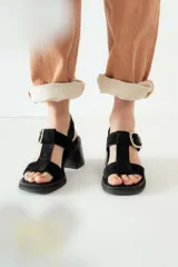 Sandalias de gamuza negra con taco cuadrado y plataforma. Presentan un diseño de tiras anchas con una hebilla metálica plateada ajustable en el lateral.