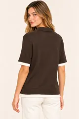 Remera polo de punto color marrón chocolate, con mangas cortas, cuello solapa y cierre frontal de botones. Cuenta con detalles en color blanco en el cuello, los puños y el ruedo, simulando un efecto de capas.
