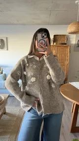 Cardigan de punto color beige con diseño de flores bordadas en relieve, cuello redondo, cierre frontal con botones y puños acanalados.