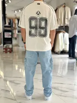 Remera regular color off-white, con diseño gráfico en la espalda que incluye el número 99 en gran tamaño y detalles en negro. Cuenta con ribetes negros en las costuras de los hombros y mangas.