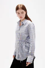 Camisa de poliéster con estampado a cuadros, cuello camisero, cierre frontal con botones y detalle de lazo ajustable en la cintura.