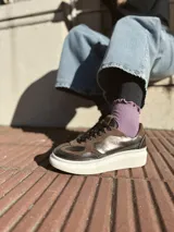 Zapatillas deportivas de cuero color peltre, con cordones negros y suela de goma blanca.