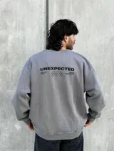 Buzo gris de corte oversize con cuello redondo y puños ajustados. Estampado en la espalda con la palabra "UNEXPECTED" y la frase "JOIN THE ROAD - POWER CONNECTION".