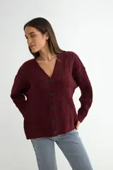 Cardigan de punto con diseño de trenzas, color bordó, con escote en V y cierre frontal de botones negros. Posee mangas largas con puños ajustados.