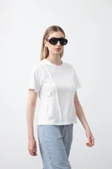 Remera de manga corta y cuello redondo, confeccionada en algodón. Presenta costuras verticales visibles en el frente que generan un efecto de entalle y estructura en la cintura.