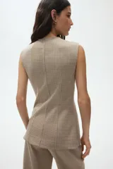 Chaleco largo sin mangas con cuello redondo y cierre frontal de botones. Presenta un diseño de tejido jacquard con patrón de cuadros pequeños y costuras verticales que definen la silueta.