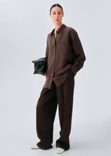 Camisa de seda de corte oversize, color marrón chocolate, con cuello camisero, mangas largas con puños abotonados y cierre frontal de botones ocultos.