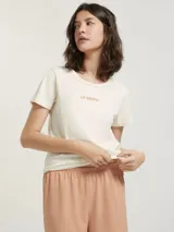 Pijama compuesto por una remera de algodón color crema con estampa pequeña en el pecho y un short de tela liviana color beige con estampado de cuadrícula fina.