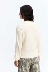 Remera de manga larga en color crema, confeccionada en tejido con textura tipo waffle. Presenta un corte relajado, cuello redondo y mangas con volumen sutil en los puños.