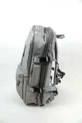 Mochila gris de poliéster, con compartimento principal con cierre, bolsillo frontal con cierre y bolsillo vertical en el frente.