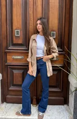 Camisa de estilo sobrecamisa en color beige, confeccionada en tela tipo gamuza o cuero sintético. Presenta cuello clásico, cierre frontal con botones, bolsillos delanteros con solapa y mangas largas con puños abotonados.