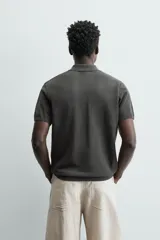 Jersey de punto color verde oliva, de calce relajado (relaxed fit), con cuello solapa y abertura frontal en forma de V. Es de manga corta y presenta acabados en rib en puños y ruedo.