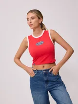 Musculosa roja de corte ajustado (tank fit) con ribetes blancos en cuello y sisas. Presenta un parche ovalado estampado en el pecho con el texto "Rusty Shop EST. IN 1985".
