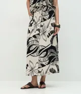 Pollera larga (midi) de corte evasé, con cintura elástica y lazo. Presenta un estampado grande en blanco y negro de motivos tropicales como hojas de palmera y flores.