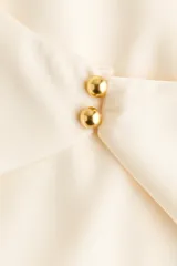 Minivestido de corte holgado en tejido fluido de satén color beige, con escote drapeado y tira halter con cierre de botones.