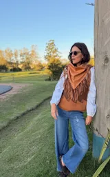 Ruana triangular de cuero ovino color suela, con flecos largos hechos a mano en todo el borde y detalle de pasamanería artesanal.