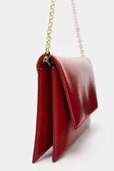 Bolso tipo bandolera de diseño estructurado, acabado brillante en color rojo y correa de cadena dorada. Cuenta con solapa frontal y doble compartimento interior.