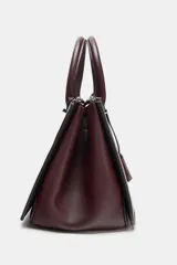 Bolso tipo mini city de diseño estructurado, con doble asa de mano y asa bandolera extraíble. Cuenta con doble compartimento exterior con cierre de cremallera metálica y un compartimento central con cierre imantado. Incluye un detalle de etiqueta colgante decorativa.
