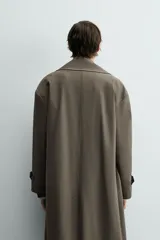 Trench color verde militar, de corte oversized, con cuello con solapas de muesca y manga larga con puño y trabilla. Presenta bolsillos de plastrón con solapa en la cadera y un bolsillo interior. Tiene una abertura en el centro de la espalda y cierre frontal de botonadura cruzada.