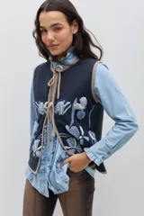 Chaleco de lana color azul marino con bordados florales artesanales en tonos azules y crudos. Presenta un cierre frontal con lazos ajustables y terminaciones en color beige.