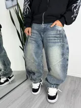 Pantalón de jean estilo baggy con lavado desgastado y diseño estampado de estilo gótico en la pierna. Presenta costuras reforzadas y corte holgado.