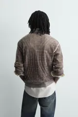 Jersey de punto con diseño jacquard abstracto, cuello redondo y manga larga. Presenta un acabado texturizado con detalles de líneas verticales y terminaciones en rib en cuello, puños y ruedo.