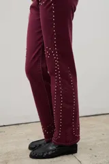 Pantalón de denim negro con diseño de tachas metálicas distribuidas en patrones curvos. Presenta un corte recto y tiro medio.