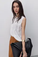 Blusa sin mangas color negro, de silueta fluida, con cuello redondo, detalle de alforzas en el frente y abotonadura parcial con botones visibles.
