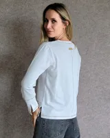 Remera blanca de manga larga con cuello en V y costuras decorativas en contraste. Incluye un lazo ajustable en el cuello con herraje metálico circular.