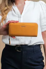 Billetera larga tipo sobre de la marca Lincoln's, confeccionada en material sintético con textura suave en color beige. Presenta un cierre perimetral metálico y el logo de la marca grabado en la parte frontal.