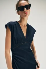 Vestido midi de denim azul oscuro, con escote en V, mangas cortas y detalles de entredoses en el escote y la cintura. Cuenta con cierre trasero con cremallera oculta.