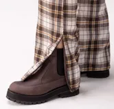 Botas negras de cuero estilo chelsea, con suela track gruesa y elásticos laterales. Presentan una tira vertical de cuero marrón en la parte posterior.