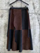 Falda midi confeccionada en 100% cuero, con diseño de paneles en bloques de color negro y chocolate. Presenta una cintura ajustable con lazo y un borde lateral con corte irregular.