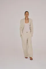 Pantalón barrel de tiro medio confeccionado en hilatura con lino, color beige con diseño a rayas sutiles. Cuenta con cintura con trabillas, bolsillos laterales ocultos en costura, pierna ancha y cierre frontal con cremallera y botón.