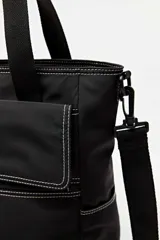 Cartera tipo tote de color negro con costuras blancas contrastantes. Posee doble asa de mano, un compartimento principal con cierre, bolsillo frontal con solapa y bolsillos laterales. Incluye además un pequeño parche con la marca y presillas laterales para correa.