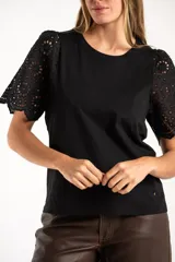 Remera de algodón peinado color negro, con mangas cortas de broderie con diseño calado y terminación festoneada. Presenta un corte oversize y cuello redondo.