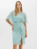 Vestido midi de tejido metalizado color turquesa, con sobrecapa de tul liviano sobre los hombros, detalle de pedrería en la cintura, volado lateral y tajo frontal.