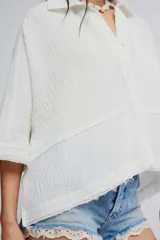 Blusa blanca de algodón vaporoso, con diseño holgado y ligeramente extragrande, cuello camisero, cierre frontal de botones y mangas amplias.