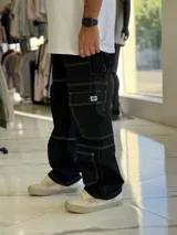 Pantalón cargo de jean negro con múltiples bolsillos utilitarios y costuras visibles en contraste de color blanco.