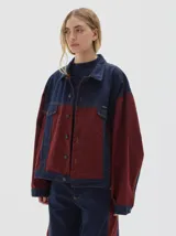 Campera tipo trucker de corte oversize, confeccionada en algodón con diseño colorblock en tonos azul marino y bordó. Presenta cierre frontal con botones metálicos, cuello clásico y bolsillos frontales con solapa.