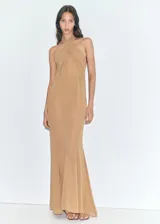 Vestido largo semitransparente de gasa color tostado, colaboración Supriya Lele x Mango, con cuello halter cruzado y drapeado, forro interior y cierre de cremallera en la parte posterior.
