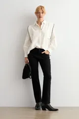 Camisa de color blanco con cuello clásico, cierre frontal de botones y mangas largas con puños. Presenta detalles de bordado geométrico en contraste a lo largo de los hombros y la parte superior de la espalda.