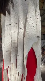 Ruana de tejido de punto color crema con diseño de líneas horizontales caladas y terminación con flecos en el ruedo.