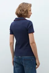 Remera de punto tipo polo color azul marino, con cuello abierto y detalles de vivo en color rojo en el borde del cuello y las mangas.