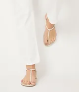 Sandalia plana de mujer color dorado metalizado, con diseño minimalista de tira fina que une la puntera y el empeine, y tira elástica fina alrededor del tobillo.