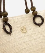 Cartera tipo bolso shopper de Bossa Nossa, confeccionada en fibra de papel color beige, con asas de hombro decoradas con cuentas de madera y aros oscuros. Cuenta con cierre de botón a presión y detalle metálico dorado frontal.