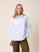 Camisa de manga larga con cuello clásico y cierre frontal de botones. Presenta un diseño de rayas verticales finas en color celeste y blanco, con un bolsillo frontal en el pecho.