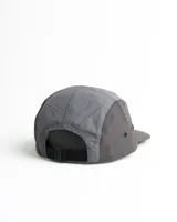 Gorro con visera de cinco paneles, combinado en gris oscuro en la visera y laterales, gris claro en el panel frontal y blanco en el panel central. Estampado frontal con el texto "The Adventure is out there" y un dibujo de montañas.