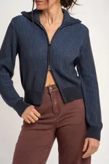Cardigan de punto acanalado en color azul marino con rayas verticales celestes, de manga larga, con cuello alto y cierre frontal con cremallera.