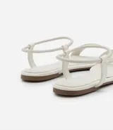 Sandalias planas blancas con tira elástica en el tobillo y tira fija sobre los dedos.